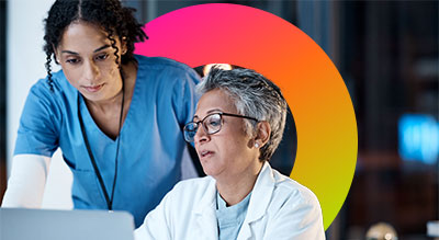 Two healthcare professionals, one in blue and the other in white, are focused on a laptop
