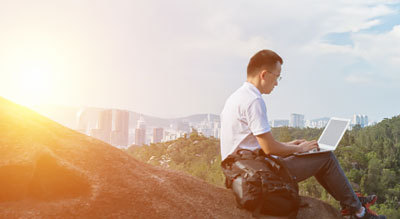 Man sitting on a hill outside of city working on laptop