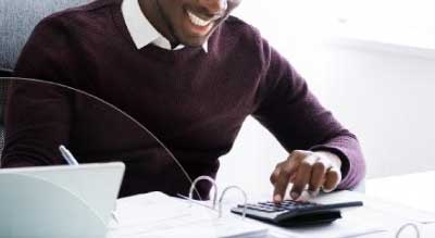 Man typing in calculator as he writes in a binder