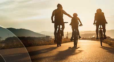 Three people ride bicycles towards a sunset