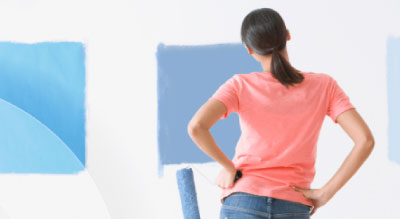 A person holding a paint roller and looking at a wall with freshly painted blue squares.