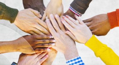 A group of hands of different colors and sizes stacked together in a gesture of unity.