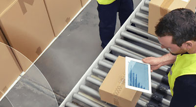 Man stands in front of packages while reviewing tablet