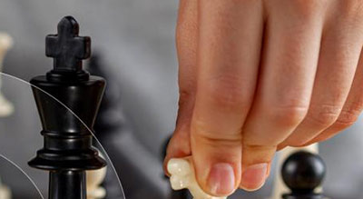 A hand moving a white knight chess piece on a chessboard, with a black king in the background.