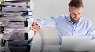 Man holding up a stack of binders while working on laptop