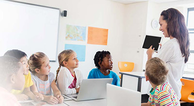 kids in classroom with teacher using laptops
