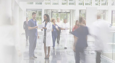 Two hospital employees talk while nurses run past them