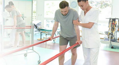 Physical Therapist assists man walking with support bars
