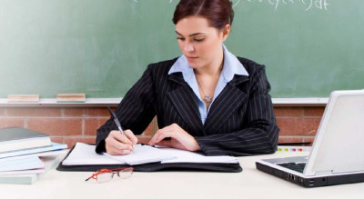 Teacheer working at desk in front of chalkboard
