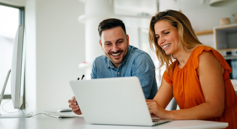 Two individuals sitting at a desk inside an office looking over a laptop