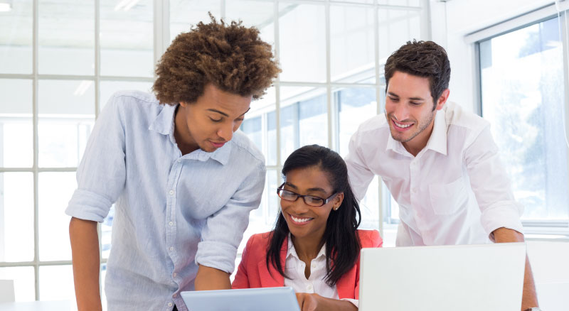 Three people working together in an office, using laptops and tablets
