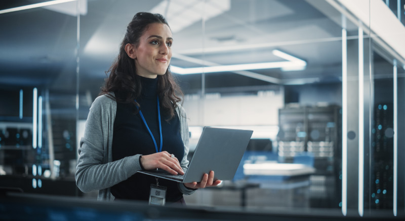 A smiling individual writes notes while using a laptop