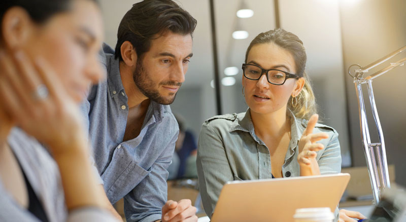 Three people engaged in a focused discussion around a laptop, highlighting teamwork and collaboration