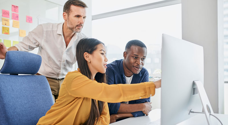 Three colleagues collaborating and discussing work in front of a computer in a bright office