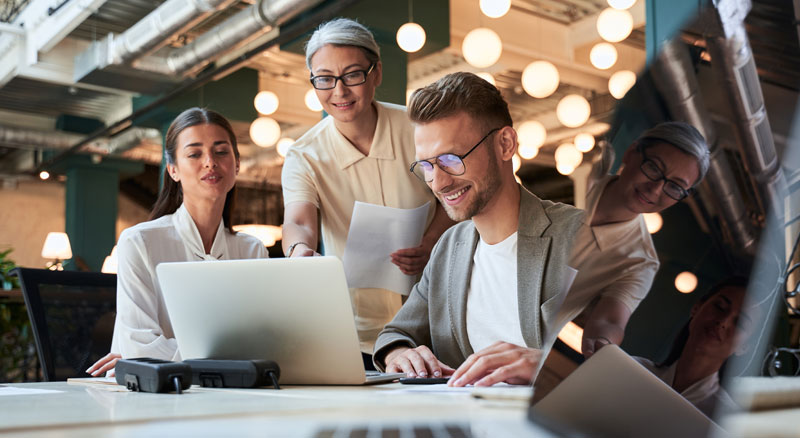 A group of professionals collaboratively working around a table with laptops and papers