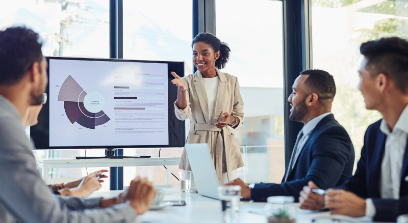 A person presenting a graphical report on a screen to three other individuals