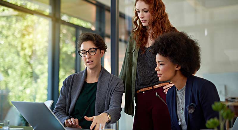 Three individuals looking at a laptop discussing governance protocols and compliance