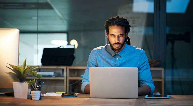 A person sitting at a desk working on a laptop in an office setting during evening hours
