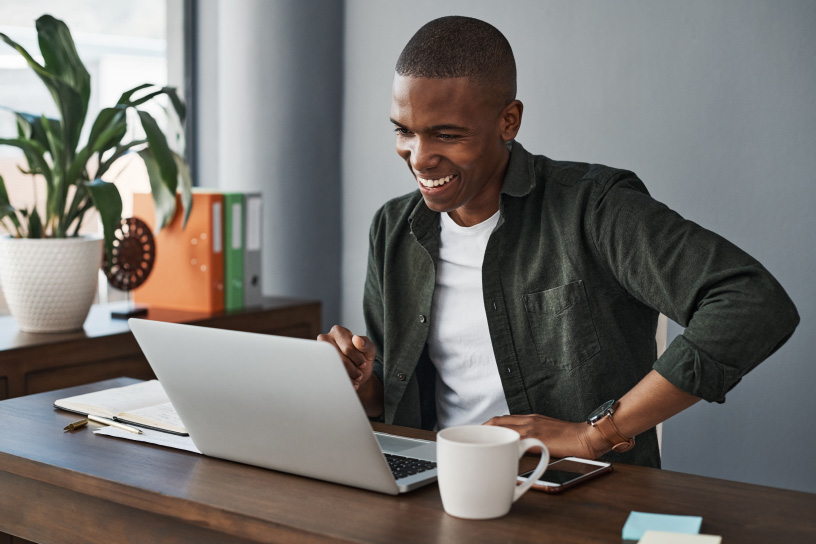 A person is using a laptop at a desk with a coffee cup and notepad