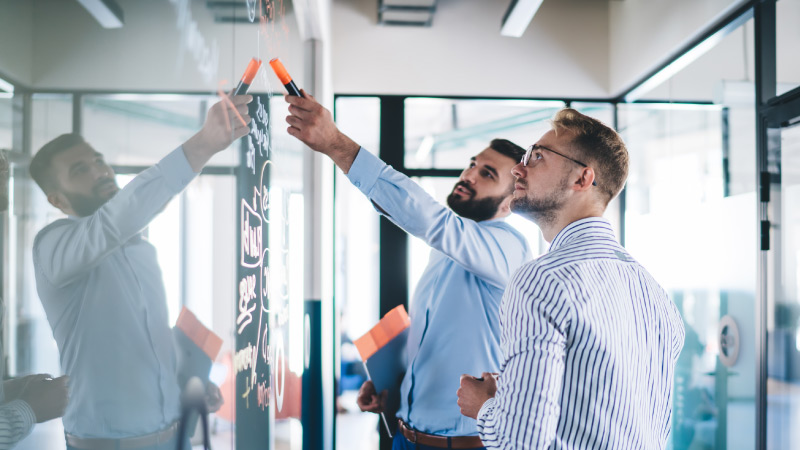 Two people are working together on a dry erase board filled with diagrams