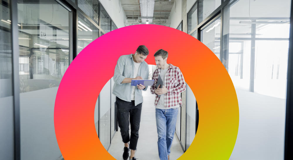 Two male employees walking down hall looking at a tablet