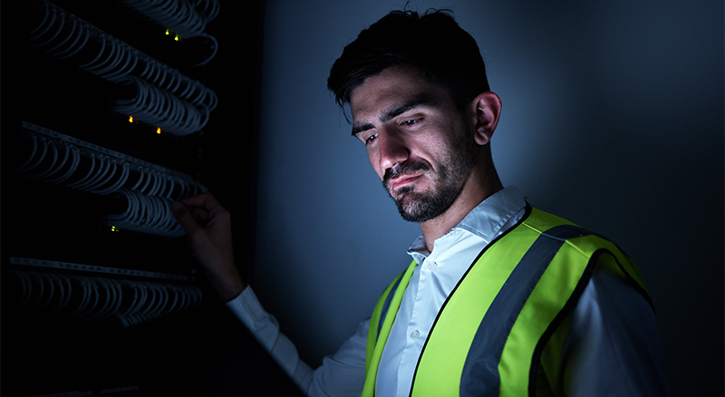 A person in a neon vest inspecting cables in a server room