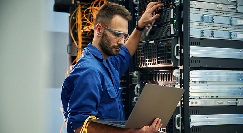A person wearing a blue shirt and glasses is focused on their work in a server room