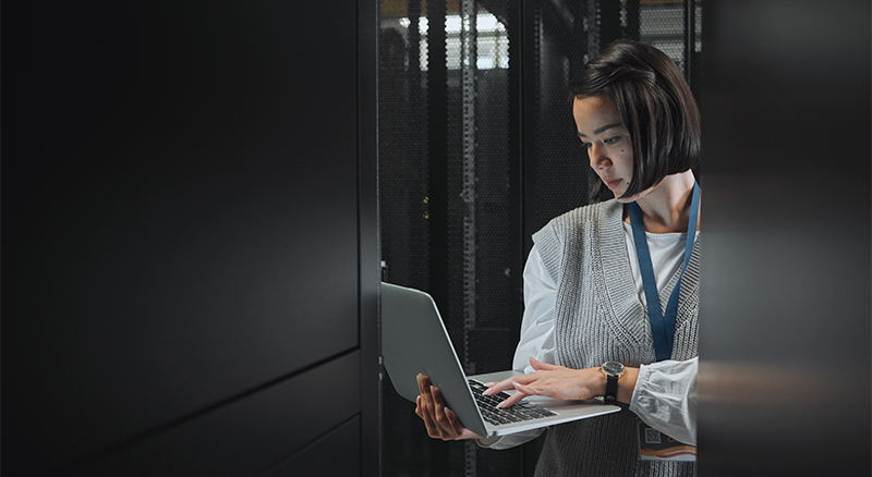 A person working on a laptop surrounded by rows of servers in a high-tech server room