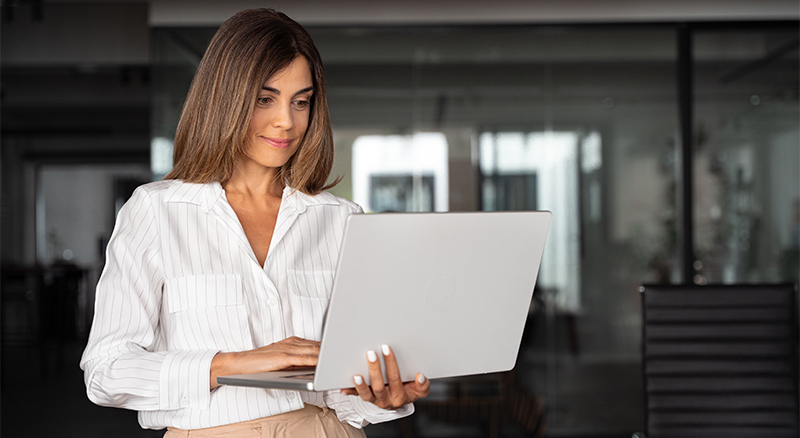 A person wearing a white shirt is holding a laptop, appearing focused and ready to tackle their work