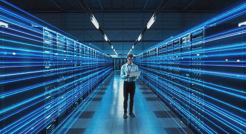 A person is positioned in a data center, bathed in blue light, highlighting the advanced technology and server equipment around him