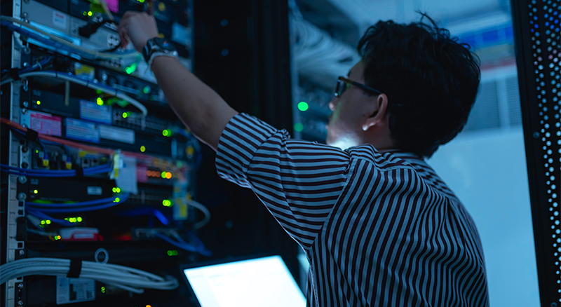 A person in a striped shirt is focused on their work in a server room.