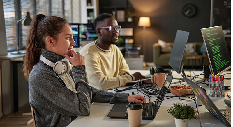 Two employeese are looking at a their devices in a workplace setting