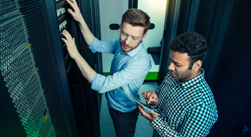 Two men in a server room and one is working on an ipad