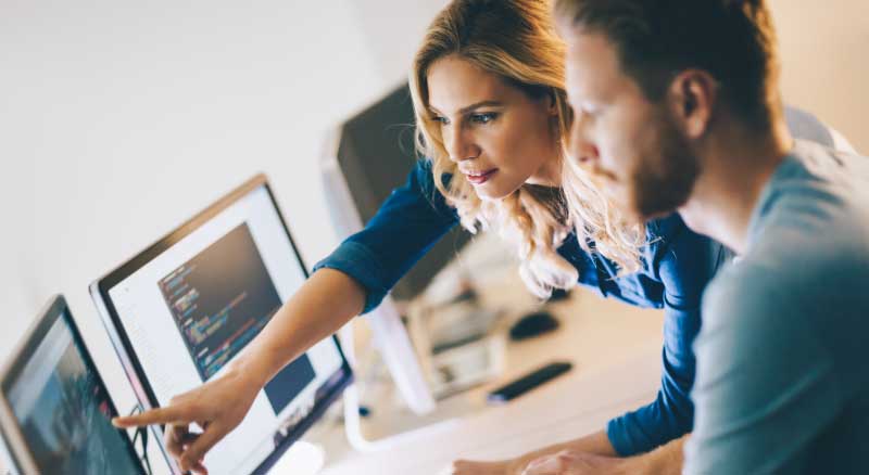 An individual working with a coworker on the computer