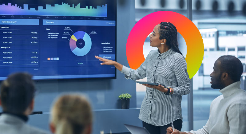 A woman leading a meeting discussing statistics on a monitor