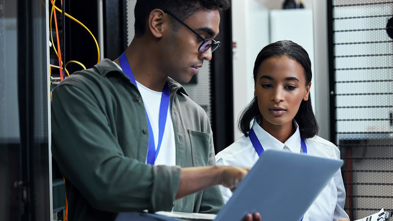 A man and woman look at a laptop infront of a networking system