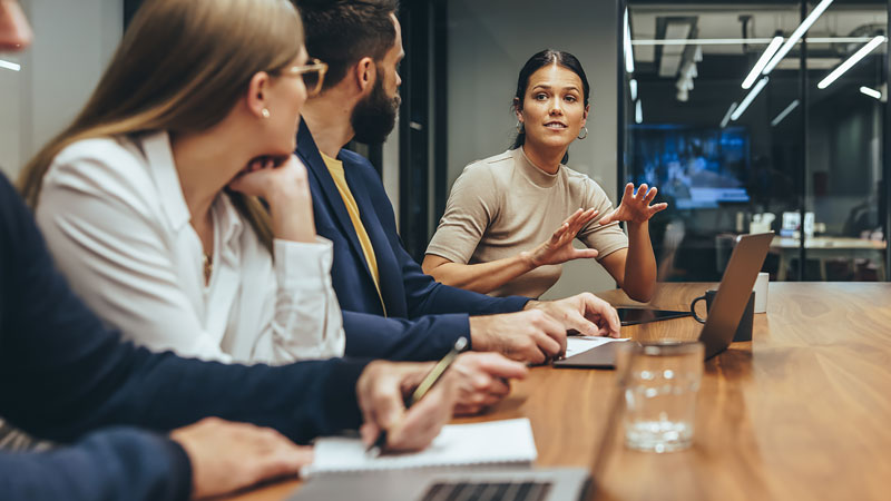 Team leader talks in a meeting while employees use laptops