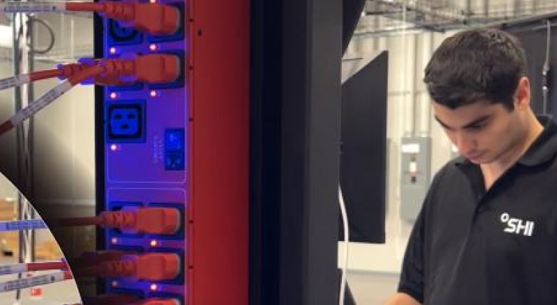 Technician in black polo shirt with ‘SHI’ logo inspecting a server rack filled with red network cables and orange boots in an industrial data center.