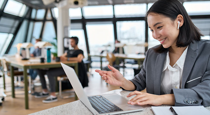 An individual talking to an open laptop wearing earbuds