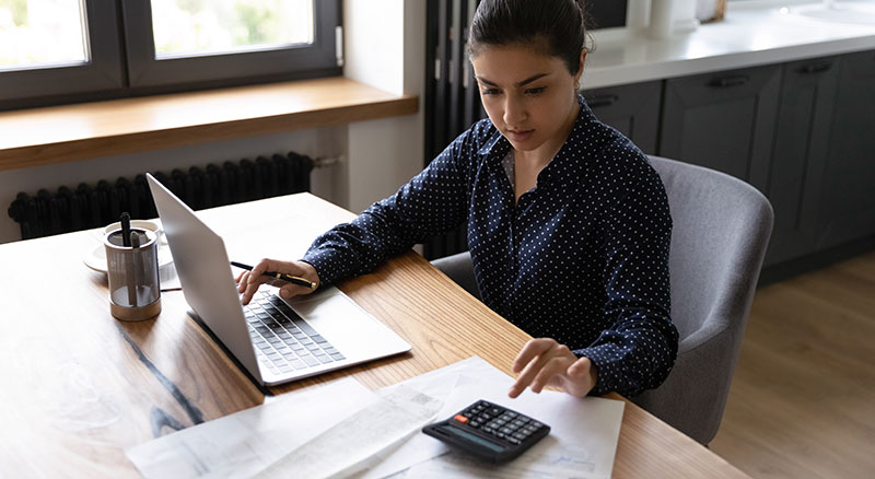 A professional uses a laptop while typing on a calculator in a modern office environment