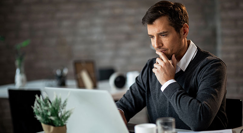 A person in deep thought while working on a laptop in a home office environment