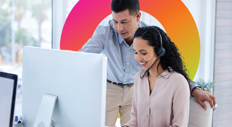 Two employees are working at a desktop computer in an office environment