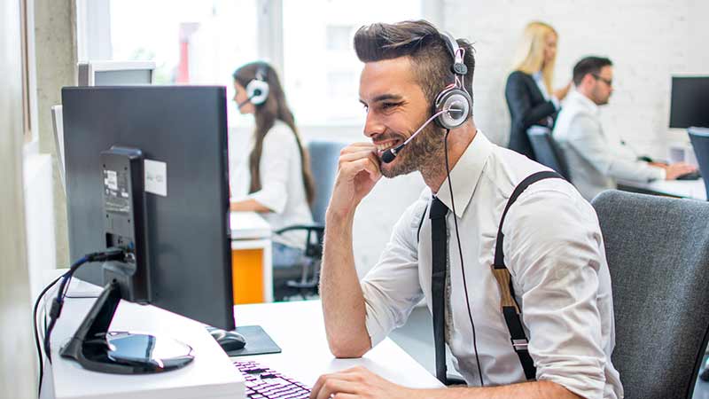 A person working at a computer in a busy office environment with headphones on