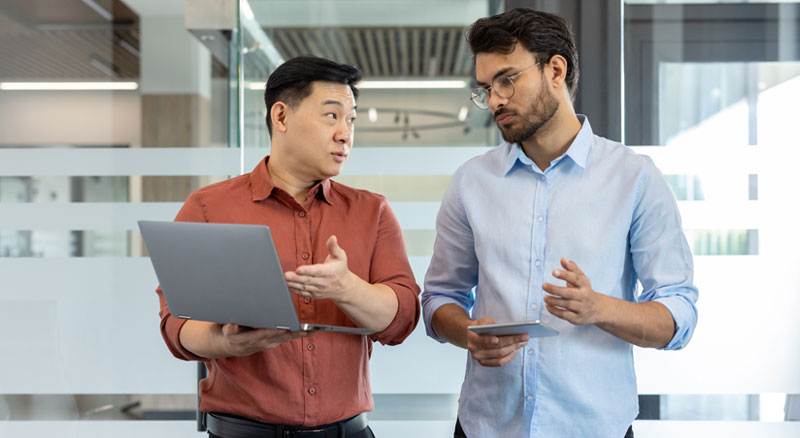 Two employees exchanges information on a laptop and tablet