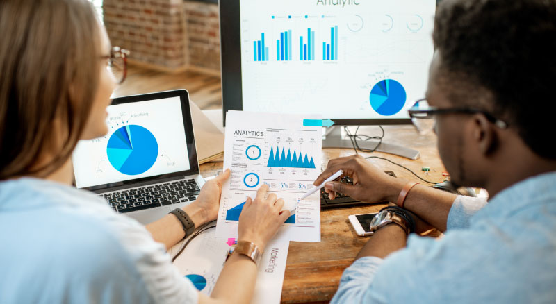 Two individuals analyzing printed and digital data charts during a business meeting