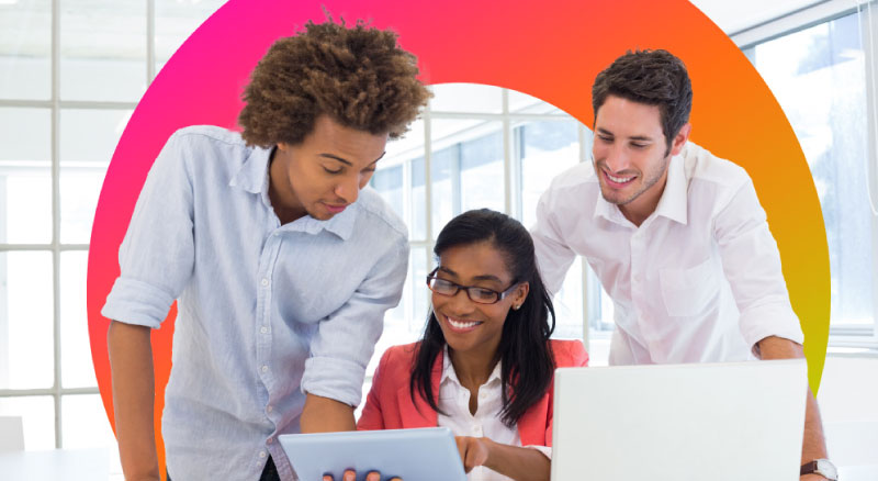 Three people huddle over a laptop and tablet