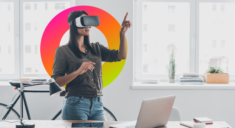 Woman in virtual reality headset pointing in the air while standing near her working place in office