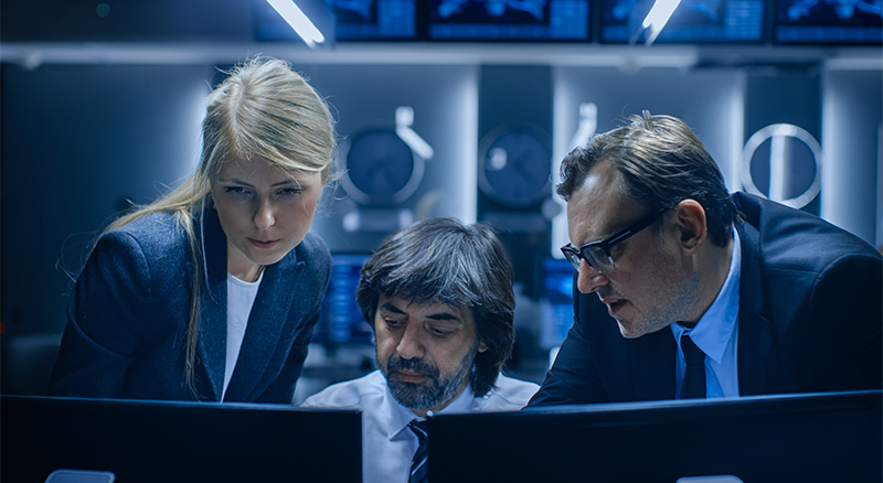 Three people in a high-tech office or control room, looking at computer screens