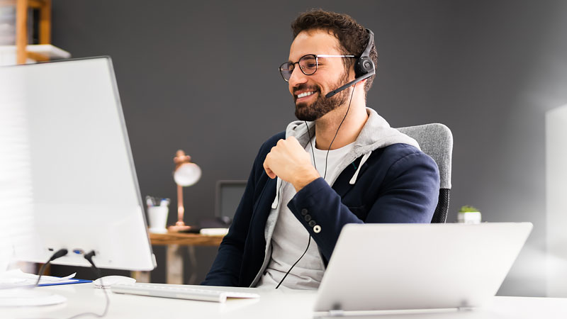 smiling man wears headset while using desktop computer