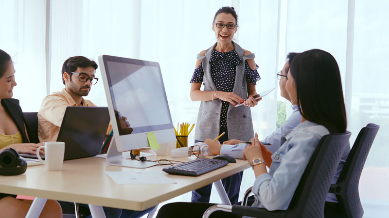 meeting of employees surrounding table with a computer